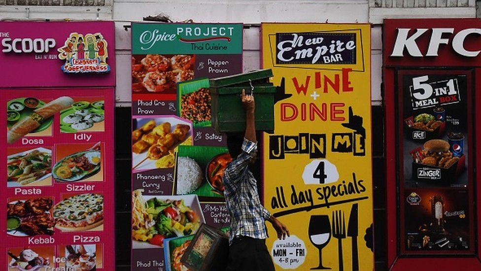 Un vendedor indio pasa junto a carteles publicitarios de restaurantes en Calcuta.