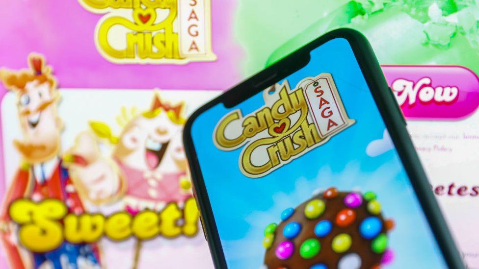 El teléfono inteligente muestra el juego Candy Crush Saga y el logo en el fondo