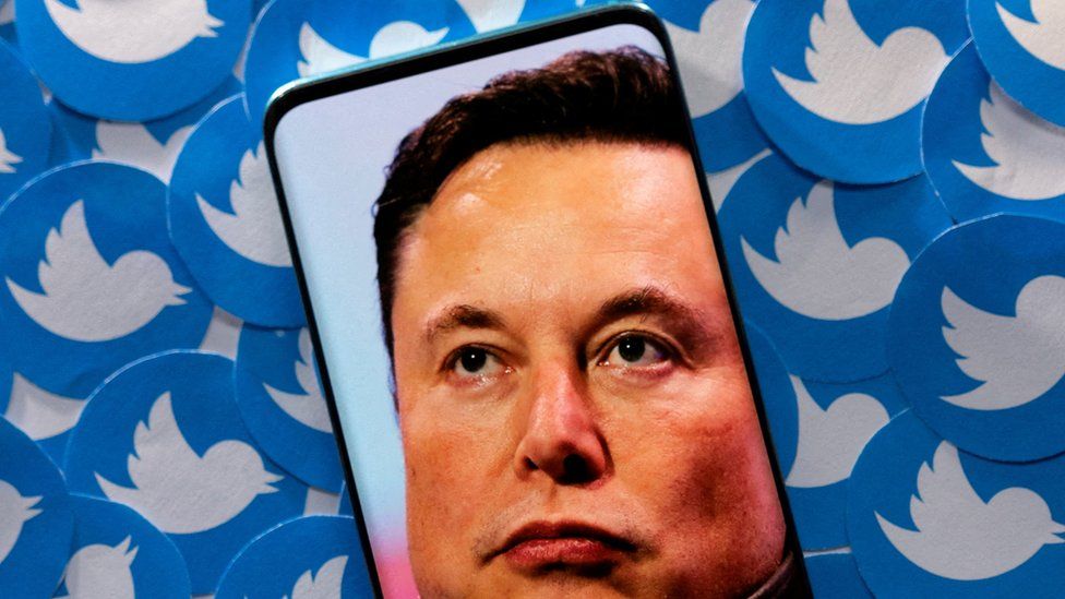 Elon Musk en la pantalla del teléfono con los logotipos de Twitter de fondo.